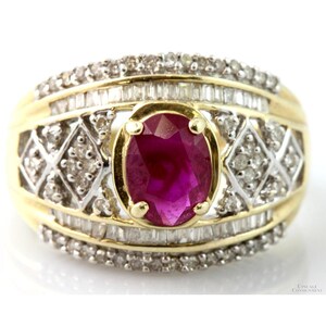 May include: A gold ring featuring a large oval ruby center stone. The ring is surrounded by smaller diamonds and baguette-cut stones. The band has a diamond-patterned design. The ring is set on a white background.