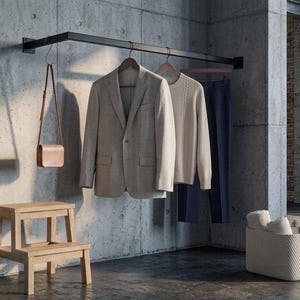 Könnte beinhalten: Eine schwarze, wandmontierte Kleiderstange aus Metall mit einem beigen Blazer, einem beigen Pullover und einer marineblauen Hose auf Holzkleiderbügeln. Eine beigefarbene Umhängetasche aus Leder hängt an der Stange. Ein Tritt aus hellem Holz und ein weißer Korb.