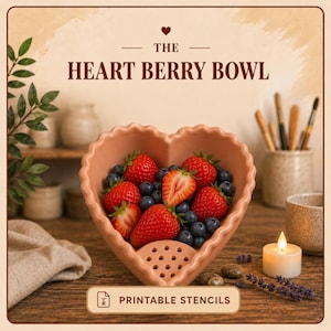 May include: A heart-shaped ceramic berry bowl in a muted terracotta color with a scalloped rim and drainage holes at the bottom. The bowl is filled with fresh red strawberries and dark blue blueberries. Text reads THE HEART BERRY BOWL and PRINTABLE STENCILS.