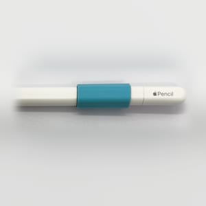 Könnte beinhalten: Ein weißer Apple Pencil Eingabestift mit einem glatten, zylindrischen Gehäuse und einer flachen Seite. Eine türkisfarbene Silikon-Griffhülle ist um die Mitte des weißen Kunststoffgehäuses angebracht, das das Apple-Logo und das Wort Pencil zeigt.