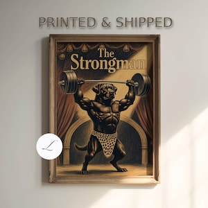 May include: A framed wall art print titled The Strongman featuring a muscular black dog wearing a leopard print loincloth, lifting a heavy barbell above its head on a stage with red curtains and a spotlight, set against a dark background.