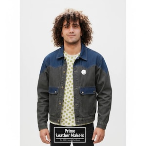 May include: A denim jacket with a two-tone design, featuring a dark gray body and blue shoulders and collar. The jacket has two front pockets and a small circular pin. The person is wearing a white t-shirt with a kiwi pattern. The text "Prime Leather Makers" is visible.