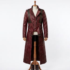 May include: A long, deep red leather coat featuring a structured collar, a front zipper closure, and dark brown textured panels on the chest. The coat includes shoulder epaulets, buckled waist straps, and quilted detailing on the upper sleeves.