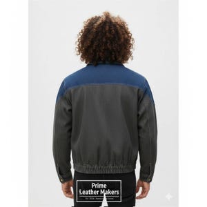 May include: A denim jacket with a two-tone design. The upper portion of the jacket is a medium blue, while the lower portion is a dark gray. The jacket has a button closure and a ribbed hem. The text "Prime Leather Makers" is visible.