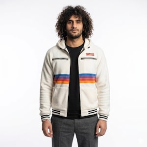 May include: Cream fleece zip-up hoodie with a retro rainbow stripe design across the chest. The jacket has black trim on the cuffs and hem, a hood, and a small logo patch. The model is wearing a black t-shirt and grey trousers.