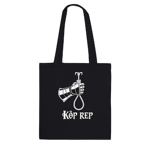May include: Black tote bag with a white graphic of a gauntlet holding a noose. The text "KÖP REP" is printed below the graphic. The bag has two black handles for carrying.