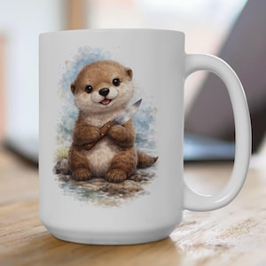 May include: A white ceramic mug featuring a watercolor-style illustration of a brown otter sitting on rocks. The otter has a light-colored belly and is holding a small silver knife with a brown handle in its front paws against a blue background.