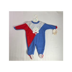 Puede incluir: Un mono de bebé de una pieza en rojo, blanco y azul, con una aplicación de oso de peluche. El mono de manga larga tiene una textura acolchada y un diseño de bloques de color diagonal. Los pies tienen un estampado de lunares.