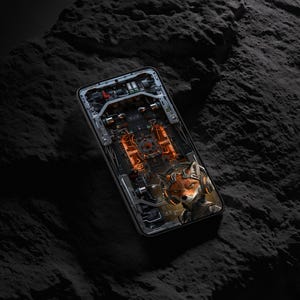 May include: A smartphone displaying a digital graphic of a fox wearing headphones against a complex mechanical background with orange glowing elements. The device features a dark frame and is positioned at an angle on a textured dark surface.
