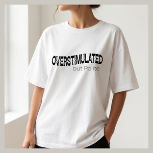 Może przedstawiać: Biała koszulka z czarnym napisem "OVERSTIMULATED but Polite". Koszulka ma krótkie rękawy i okrągły dekolt. Modelka ma na sobie czarne spodnie.