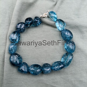 Op de afbeelding: Een blauwe kralenarmband met een zilveren sluiting. De kralen zijn doorschijnend blauw met een marmer effect. De armband ligt op een lichtgroene stof. De tekst "awariyaSethFinds" is zichtbaar.