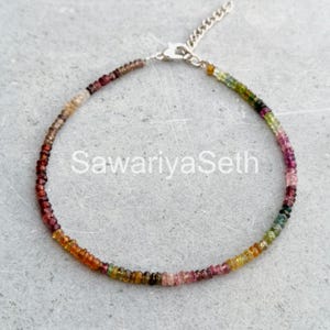 May include: A delicate bracelet featuring a strand of small, colorful beads in shades of red, orange, yellow, green, and pink. The bracelet is connected with a silver chain and clasp. The text "SawariyaSeth" is visible on the image.