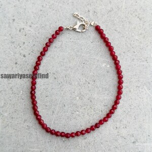 May include: A delicate red beaded bracelet with a silver-colored clasp. The beads are small and faceted, reflecting light. The bracelet is displayed on a gray surface. The text "sawariyasefind" is visible in the lower left corner.