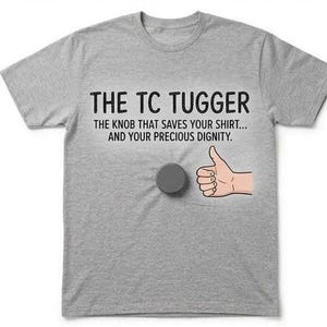 May include: A heather gray short-sleeve t-shirt featuring the black text THE TC TUGGER THE KNOB THAT SAVES YOUR SHIRT... AND YOUR PRECIOUS DIGNITY. A dark gray circular knob is attached to the center, next to a graphic of a hand giving a thumbs up.
