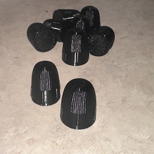 Pode incluir: Uma coleção de objetos pretos em forma de cone com uma superfície texturizada. Os objetos estão dispostos em uma pilha e espalhados em uma superfície de cor clara. Os objetos parecem ser feitos de plástico.