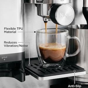May include: A black, rectangular, flexible TPU mat with an anti-slip surface designed to reduce vibration and noise. The mat is positioned under a clear, double-walled glass mug being filled with espresso from a stainless steel Ninja coffee machine.