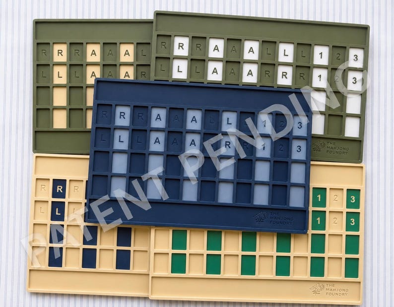 Op de afbeelding: Een collectie rechthoekige siliconen mahjong-tegelhouders in olijfgroen, marineblauw en beige. Elke houder heeft een raster van verzonken sleuven, sommige met tegels met de letters R, L, A en de cijfers 1, 2, 3. Het logo van Mahjong Foundry is in reli&euml;f aangebracht.
