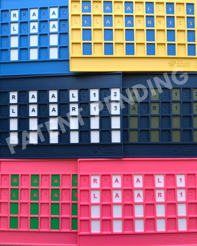 Op de afbeelding: Een verzameling van zes rechthoekige mahjong-tegelhouders in blauw, geel, donkerblauw en roze. Elke houder heeft een raster van sleuven met witte, groene of donkere inzetstukken. De letters R, L, A en de cijfers 1, 2, 3 zijn op de inzetstukken gedrukt.