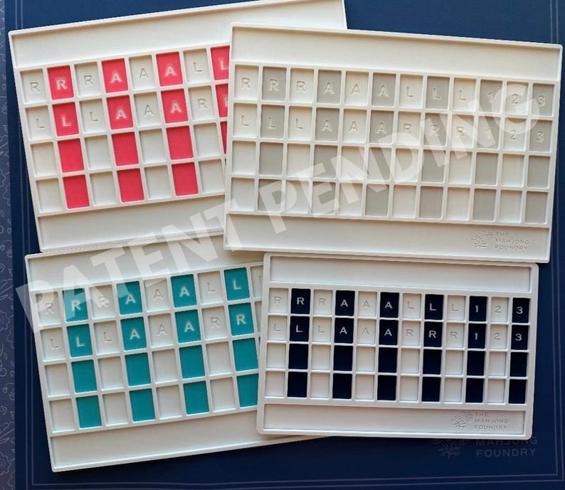 Op de afbeelding: Vier rechthoekige witte plastic spelborden met rastervakken. Elk bord bevat kolommen met gekleurde tegels in rood, grijs, groenblauw of zwart, met de letters R, A, L en de cijfers 1, 2, 3 in reli&euml;f op de tegels aangebracht.