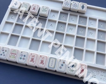 Könnte beinhalten: Ein weißer Mahjong-Fliesenhalter aus Kunststoff mit einem Gitter aus leeren Fächern und mehreren rechteckigen Fliesen an den oberen und unteren Rändern. Die Fliesen zeigen verschiedene bunte Illustrationen, chinesische Schriftzeichen und das Wort SOAP.