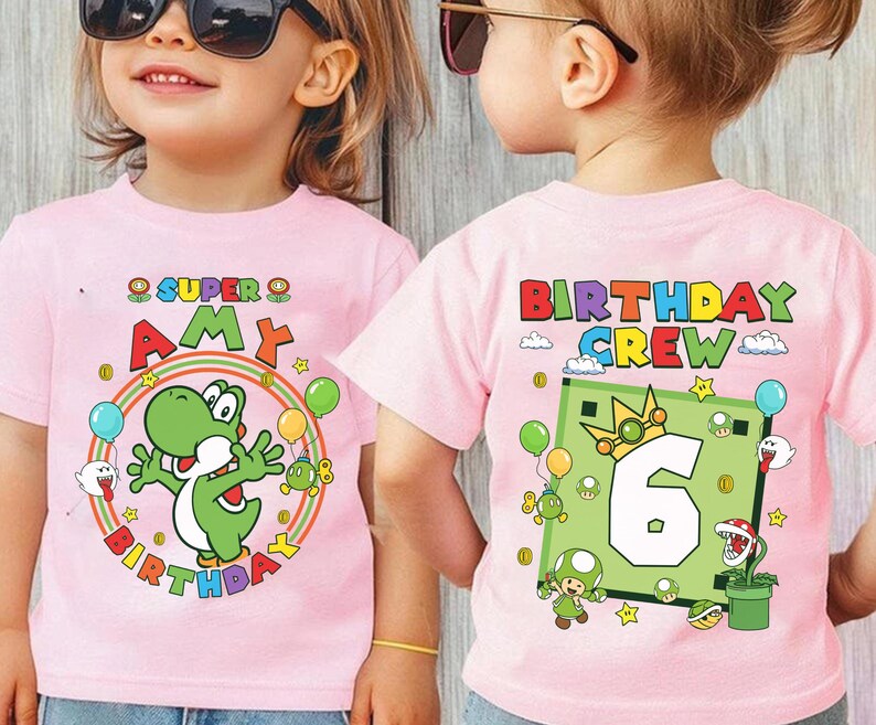 May include: Pink t-shirts with colorful graphics. One shirt features a green Yoshi character and the text "SUPER AMY BIRTHDAY". The other shirt displays "BIRTHDAY CREW" and a number 6 design with cartoon characters.