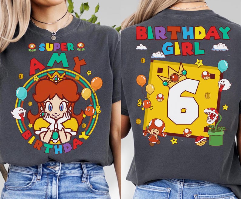 May include: Dark gray t-shirt featuring a colorful graphic of a cartoon princess with the text "SUPER AMY BIRTHDAY" on the front. The back of the shirt has "BIRTHDAY GIRL" and the number "6". Balloons and stars are also featured.