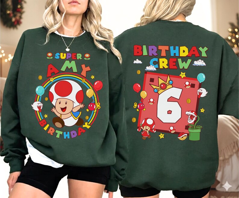 May include: Dark green sweatshirt featuring a colorful graphic of a mushroom character, a rainbow, and the text "SUPER AMY BIRTHDAY" on the front. The back of the sweatshirt has the text "BIRTHDAY CREW" and a large number "6".