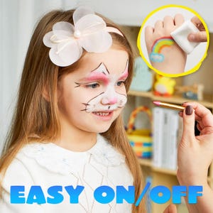Op de afbeelding: Een meisje met kattengezichtsverf, draagt een witte top en een bloemenhoofdband. De afbeelding bevat de tekst "EASY ON/OFF" in het blauw. Een hand veegt een regenboogtattoo af.