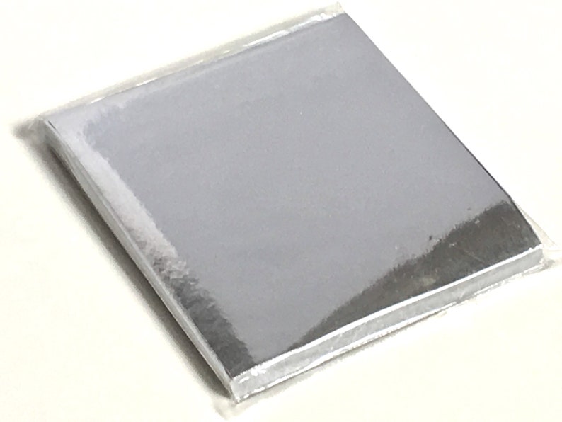 May include: A stack of silver-colored, square sheets, possibly paper or cardstock, is sealed in clear plastic. The sheets have a reflective, metallic appearance. The packaging is transparent, allowing a clear view of the contents.