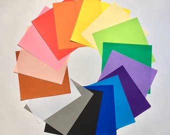 May include: A circular arrangement of coloured square paper sheets. The colours include red, orange, yellow, green, blue, purple, pink, brown, grey, black, and white. The papers are arranged in a spectrum, creating a vibrant and artistic display.