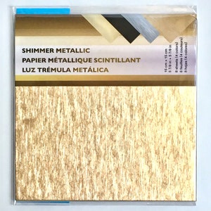 Op de afbeelding: Een pakketje goudkleurig shimmer metallic papier met een getextureerd oppervlak. Het pakket bevat 8 vellen in 4 kleuren, elk 15 cm bij 15 cm. De verpakking toont de tekst "SHIMMER METALLIC".
