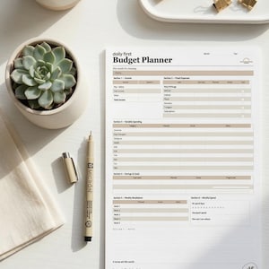 Puede incluir: Vista superior de un planificador de presupuesto con el texto "daily first Budget Planner". También hay una planta suculenta, una taza de café y artículos de papelería.
