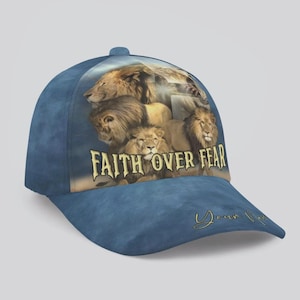 以下が含まれることがあります： ライオンのグラフィックと「FAITH OVER FEAR」の文字が入った青い野球帽。帽子にはカーブしたつばとボタンが付いています。デザインには、つばにパーソナライズされた署名が含まれています。