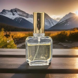 May include: A square-shaped clear glass perfume bottle with a metallic gold cylindrical cap. The bottle contains a pale yellow liquid and features a visible internal spray tube extending from the top down to the base of the glass container.