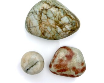 May include: Three polished stones of varying shapes and colors. The largest is a rounded triangle with a green and brown mottled pattern. A small sphere and a rounded stone with red and tan markings are also present.