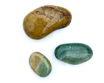 May include: Three polished stones in shades of brown, green, and tan. The largest stone is a mottled brown with darker brown and red markings. The other two stones are oval-shaped, with one being a solid teal color and the other a mix of tan and green.