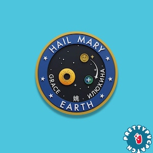 May include: A round patch with a blue border and gold trim, featuring the words "HAIL MARY" and "EARTH". The center has a bagel, a "+" symbol, and other symbols. The patch is on a light blue background.