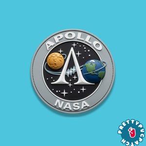 May include: A circular patch featuring the Apollo NASA mission emblem. The design includes a large white letter A, a golden moon, and a blue and green Earth against a black background with white stars. The words APOLLO and NASA are in white.