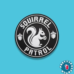 May include: A round, black and white patch with the words "SQUIRREL PATROL" encircling a white squirrel holding a nut. Two white acorns flank the squirrel. The patch has a white border and is set against a light blue background.