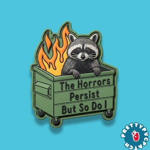 May include: A patch featuring a raccoon in a dumpster with flames. The dumpster is green, and the raccoon is gray and black. Text on the dumpster reads "The Horrors Persist But So Do I."