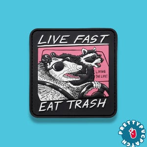May include: Black square patch with the text "LIVE FAST EAT TRASH" above a cartoon illustration of an opossum and raccoon wearing sunglasses. The opossum is driving a car with the raccoon in the passenger seat. The text "LIVING THE LIFE!" is also included.
