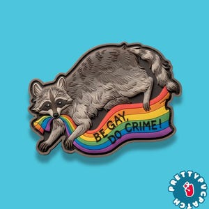 May include: A gray raccoon patch with a rainbow-colored banner that reads "BE GAY, DO CRIME!". The raccoon is holding a rainbow in its mouth. The patch has a black border and a blue background.