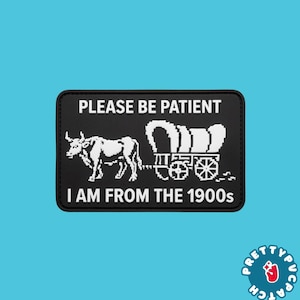 May include: A rectangular black patch with white pixelated graphics and text. The top text reads PLEASE BE PATIENT and the bottom text reads I AM FROM THE 1900s. Between the lines is a white graphic of an ox pulling a covered wagon.
