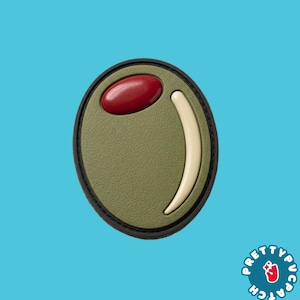 May include: An oval-shaped patch featuring a textured olive green surface, a smooth red oval accent at the top, and a curved cream-colored crescent shape. The patch is outlined with a thin black border and includes the text Pretty Patch.