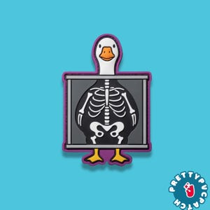 May include: A novelty patch featuring a cartoon duck with a skeleton visible inside a gray rectangle. The duck has a white head, orange beak, and yellow feet. The patch has a purple border and is set against a blue background.