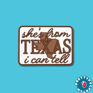 May include: A rectangular patch with a white background and a brown border. The text reads "she's from TEXAS i can tell" in brown lettering. A brown silhouette of the state of Texas is positioned behind the word TEXAS in the center.