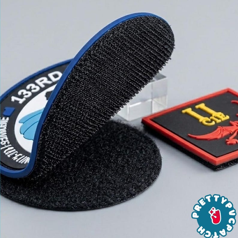 May include: Close-up of two embroidered patches. One is a circular patch with the text "133RD" and a blue border. The other is a rectangular patch with the text "II" and a red and yellow design. Both patches have a hook and loop backing.