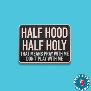 May include: A black and pink patch with the text "HALF HOOD HALF HOLY THAT MEANS PRAY WITH ME DON'T PLAY WITH ME". The patch has a black border and is set against a light blue background.