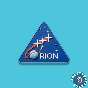 May include: A blue triangular patch featuring a stylized design with white stars, a planet, and the word "ORION." An orange arc curves around the planet. The patch has a white border and is set against a light blue background.