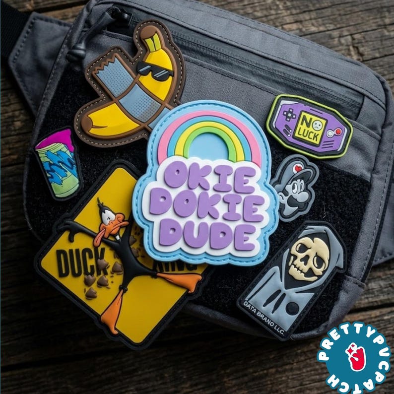 May include: A gray tactical fanny pack with several embroidered patches. Patches include a banana wearing sunglasses, a rainbow with the words "Okie Dokie Dude", and a cartoon duck. Other patches feature a video game controller and a grim reaper.
